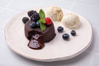 Plate with delicious chocolate fondant, berries, ice cream and mint on white tiled table