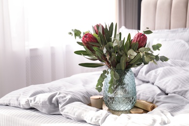 Photo of Vase with bouquet of beautiful Protea flowers on bed indoors