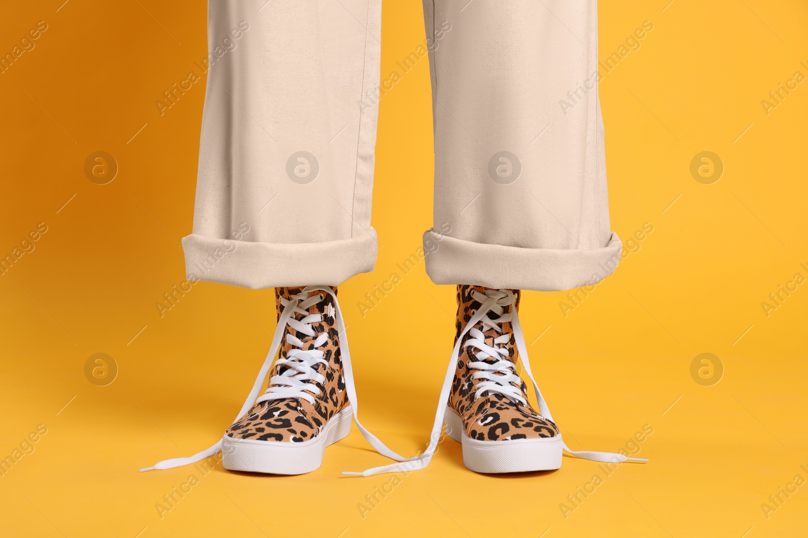 Photo of Woman wearing classic old school sneakers with leopard print on orange background, closeup