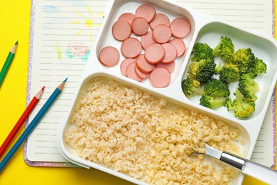 Section plate with tasty pasta, broccoli and sausage on yellow background, flat lay