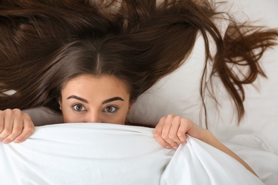 Photo of Young woman lying under blanket, top view. Bedtime