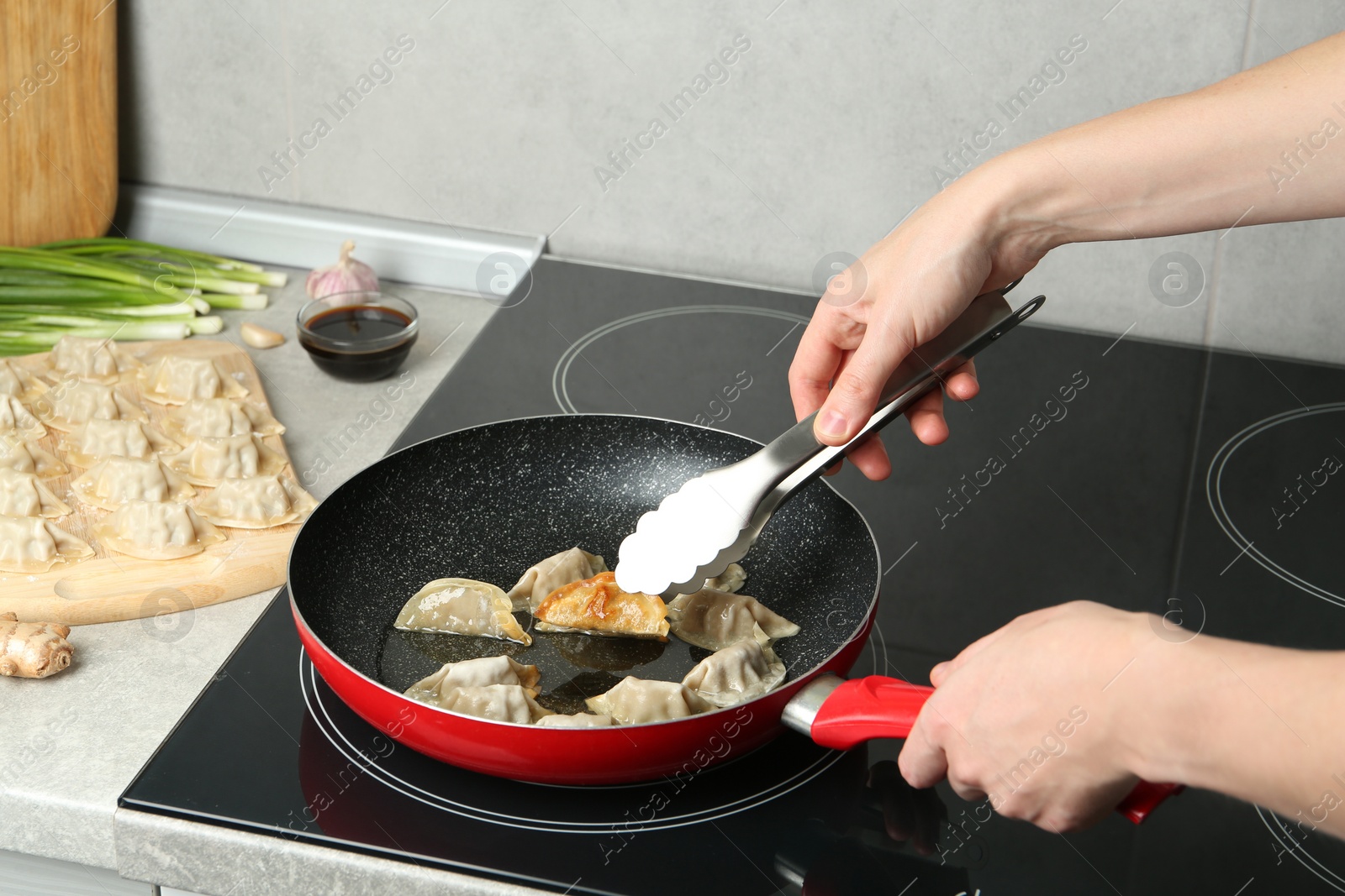 Photo of Woman cooking gyoza on frying pan with hot oil in kitchen, closeup