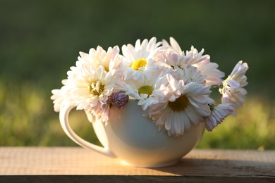 Photo of Beautiful wild flowers in cup on wooden table against blurred background, closeup