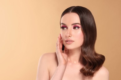 Photo of Portrait of beautiful young woman with makeup and gorgeous hair styling on beige background. Space for text
