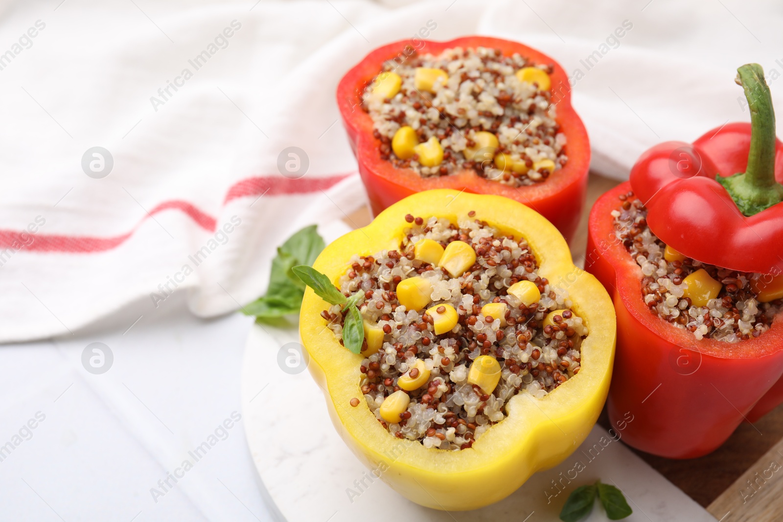 Photo of Quinoa stuffed bell peppers and basil on white table, closeup. Space for text