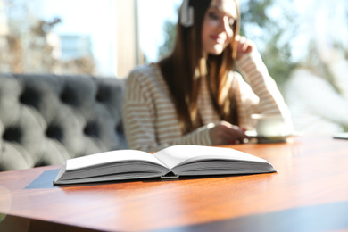 Photo of Book on table in cafe and woman with headphones on background. Audiobook concept