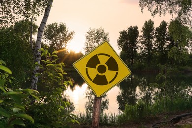 Image of Radioactive pollution. Yellow warning sign with hazard symbol near contaminated area outdoors