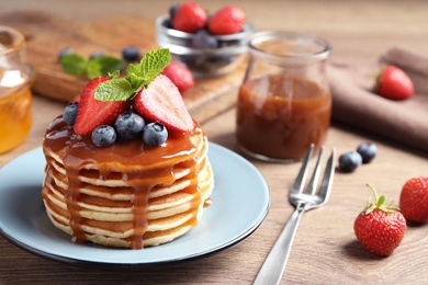 Delicious pancakes with fresh berries and syrup on wooden table