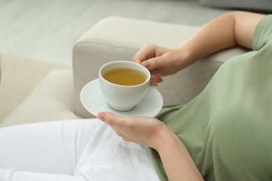 Photo of Young woman with cup of hot tea relaxing on sofa, closeup