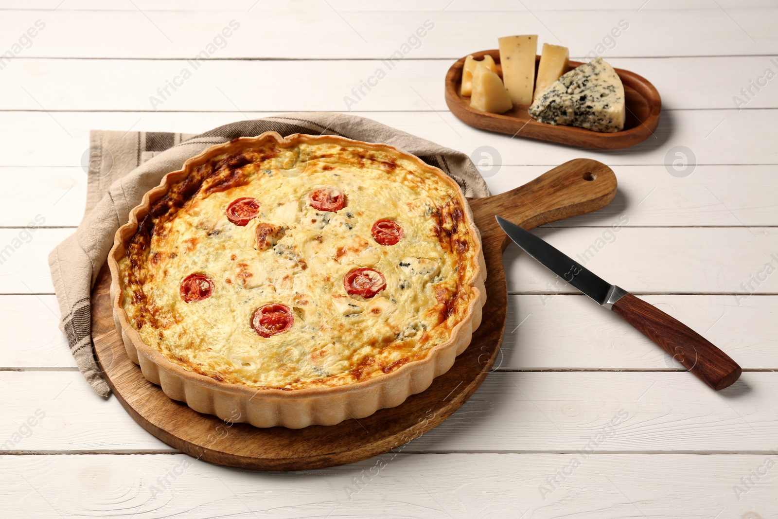 Photo of Delicious homemade cheese quiche, knife and ingredients on white wooden table