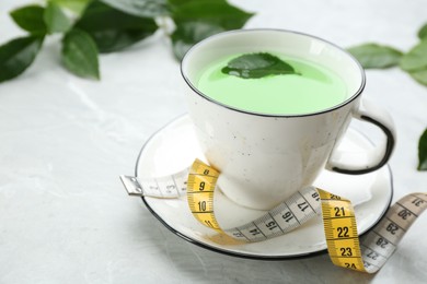 Cup of herbal diet tea and measuring tape on light table. Space for text