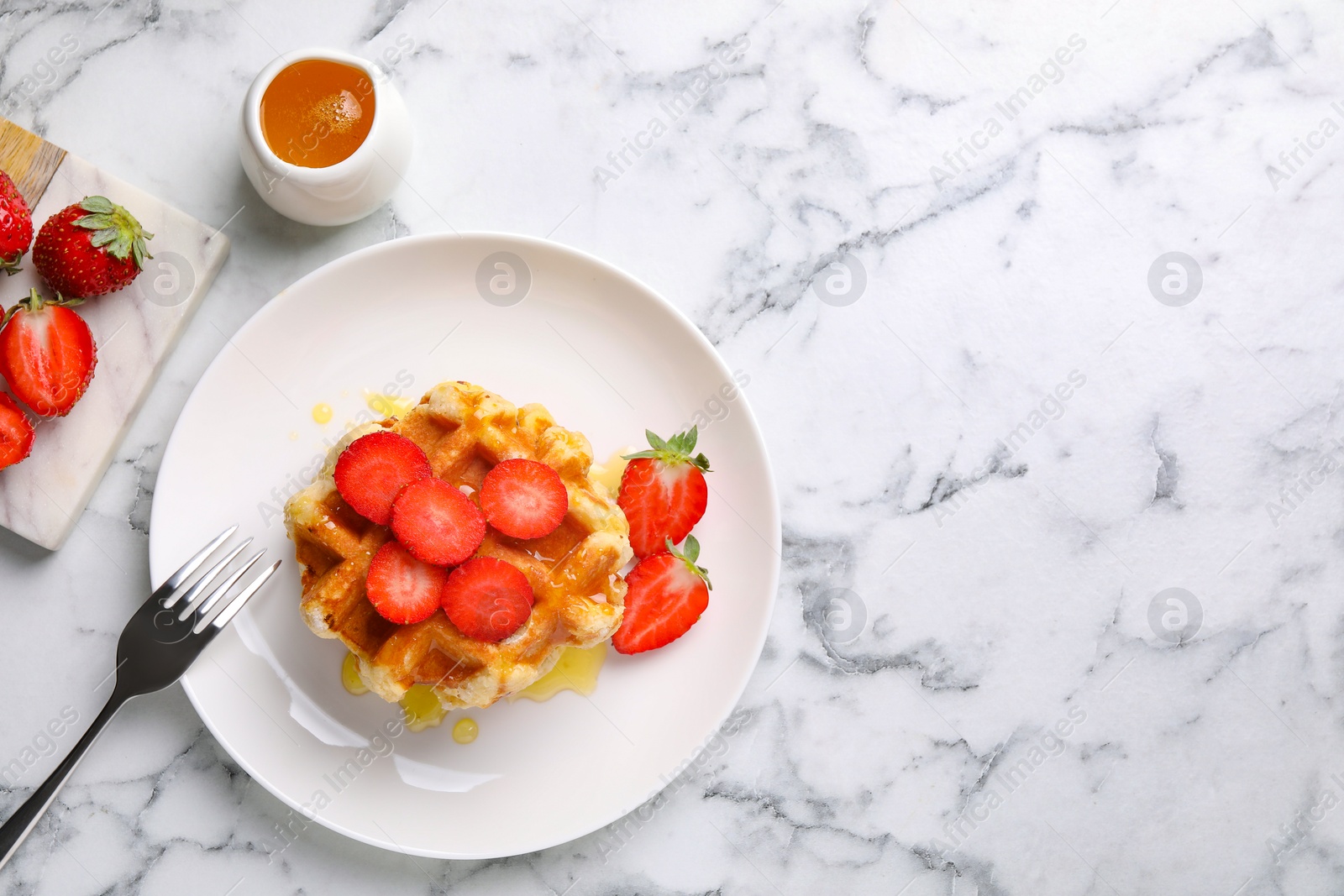 Photo of Delicious Belgian waffles with strawberries and honey on white marble table, top view. Space for text