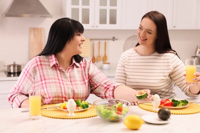 Happy overweight women having healthy meal together at table in kitchen