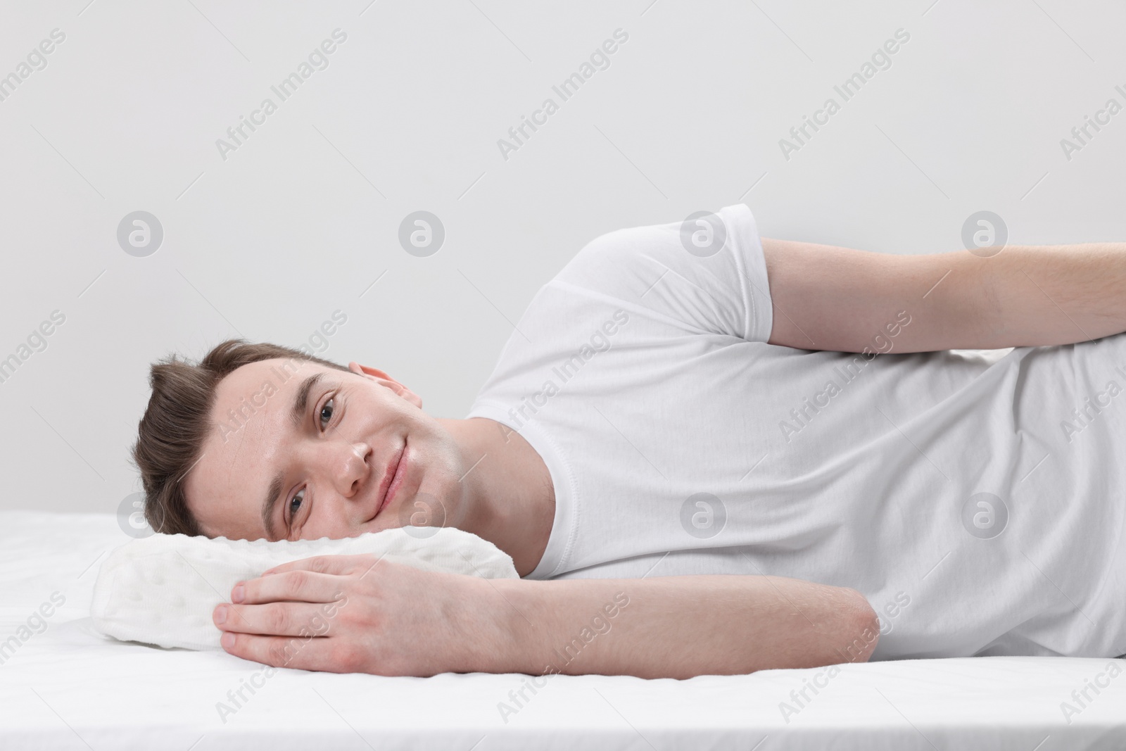 Photo of Man lying on orthopedic pillow against light grey background