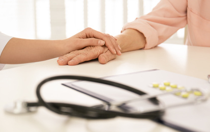 Doctor holding senior patient's hand in office , closeup