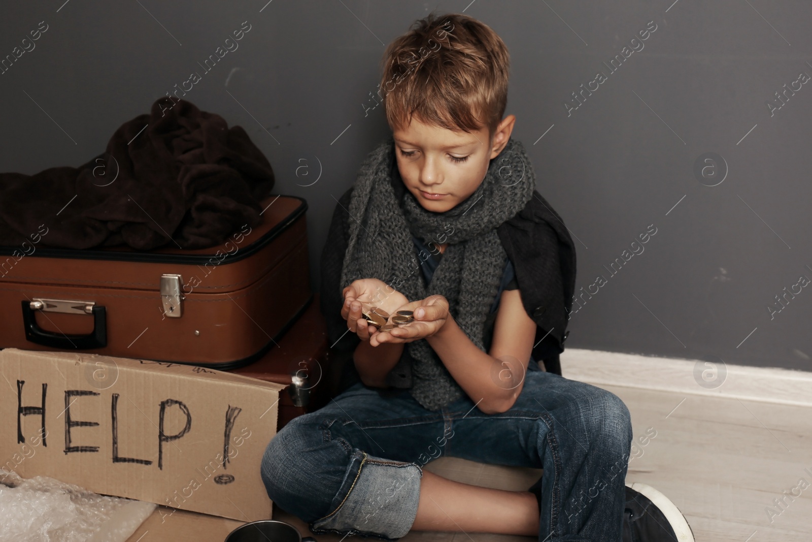 Photo of Poor homeless boy begging on floor near dark wall