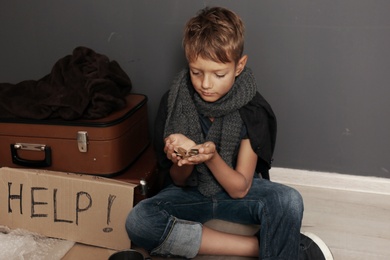 Photo of Poor homeless boy begging on floor near dark wall