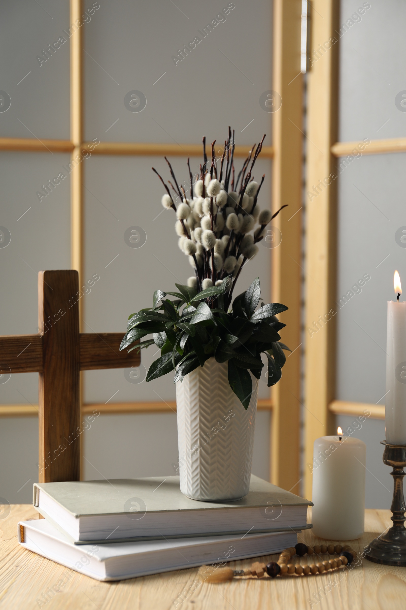 Photo of Cross, burning candles, books, rosary beads and bouquet with willow branches on wooden table