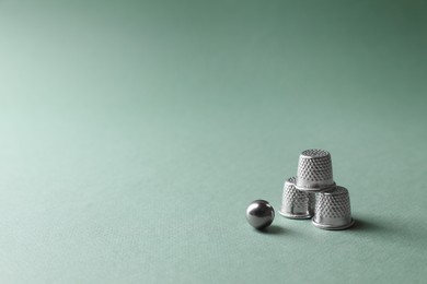 Photo of Metal thimbles and ball on pale olive background, space for text. Thimblerig game