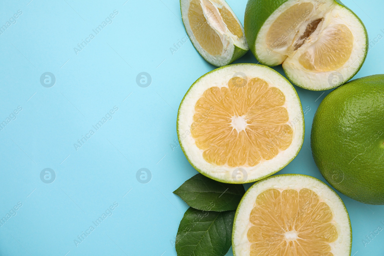 Photo of Whole and cut sweetie fruits with green leaves on light blue background, flat lay. Space for text