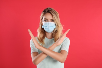 Photo of Woman in protective face mask showing stop gesture on red background. Prevent spreading of coronavirus