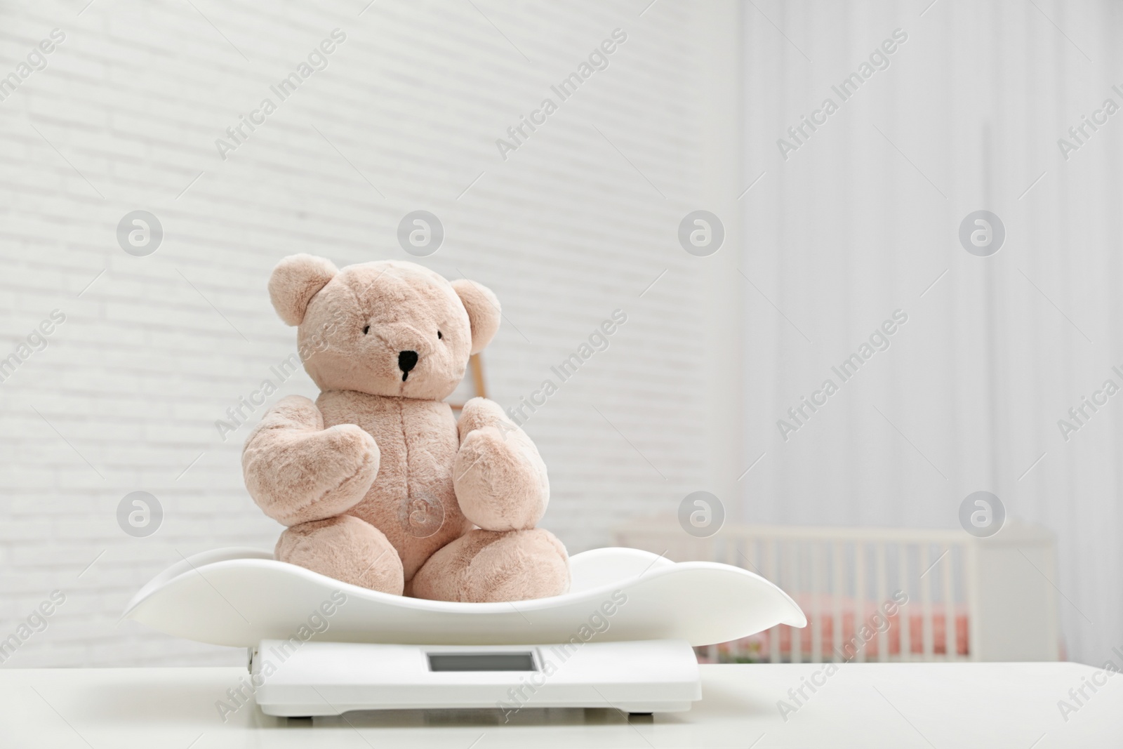 Photo of Baby scales with teddy bear on table in light room. Space for text
