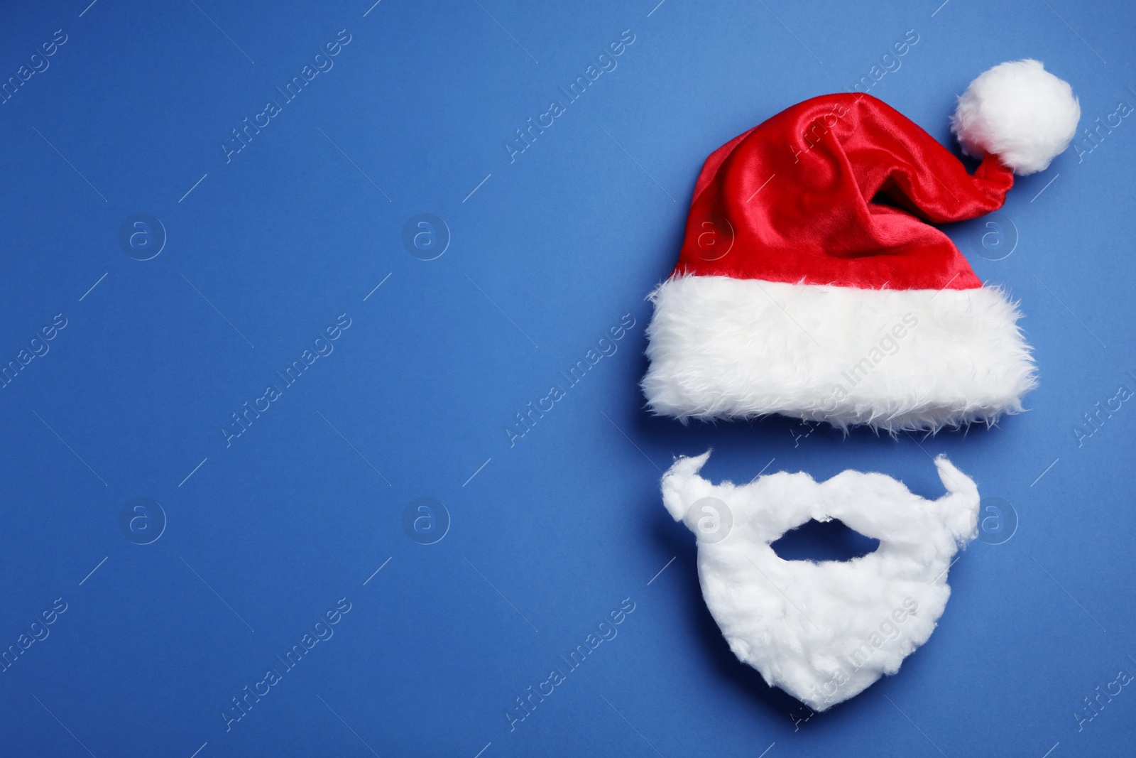 Photo of Santa Claus hat and beard on blue background, flat lay. Space for text