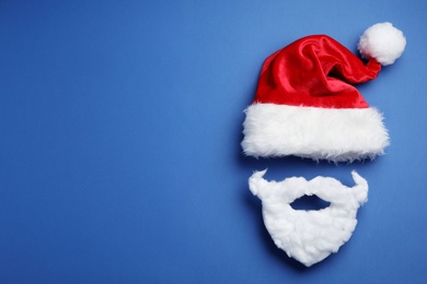 Photo of Santa Claus hat and beard on blue background, flat lay. Space for text