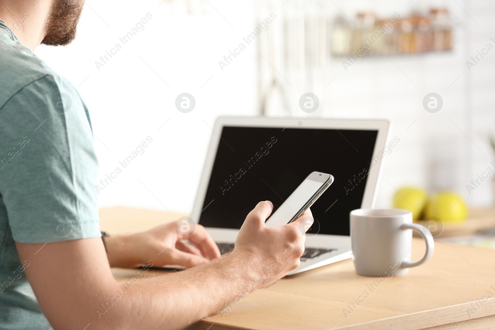 Photo of Young man using mobile phone and laptop at table