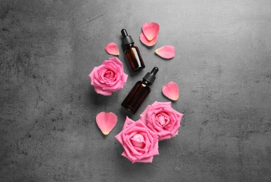 Fresh flowers, petals and bottles of rose essential oil on gray background, flat lay