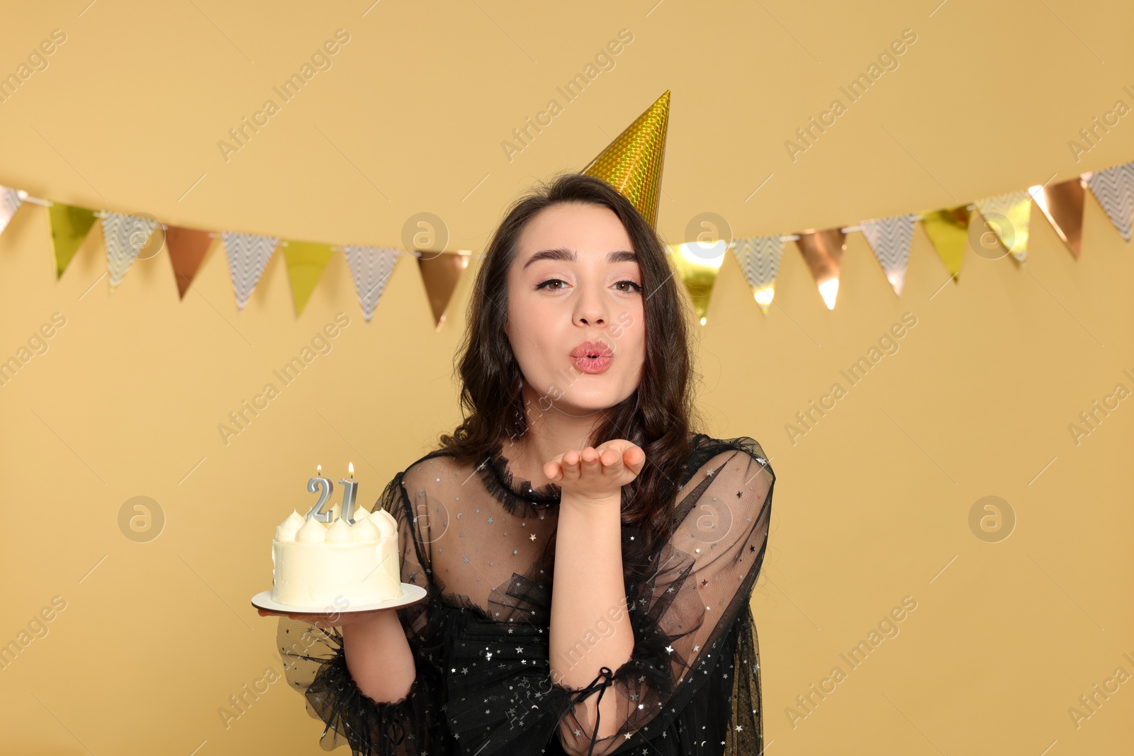 Photo of Coming of age party - 21st birthday. Woman holding delicious cake with number shaped candles and sending air kiss on beige background