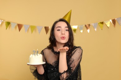 Photo of Comingage party - 21st birthday. Woman holding delicious cake with number shaped candles and sending air kiss on beige background