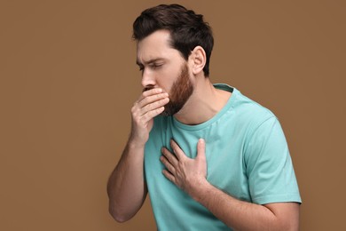 Photo of Sick man coughing on brown background. Cold symptoms