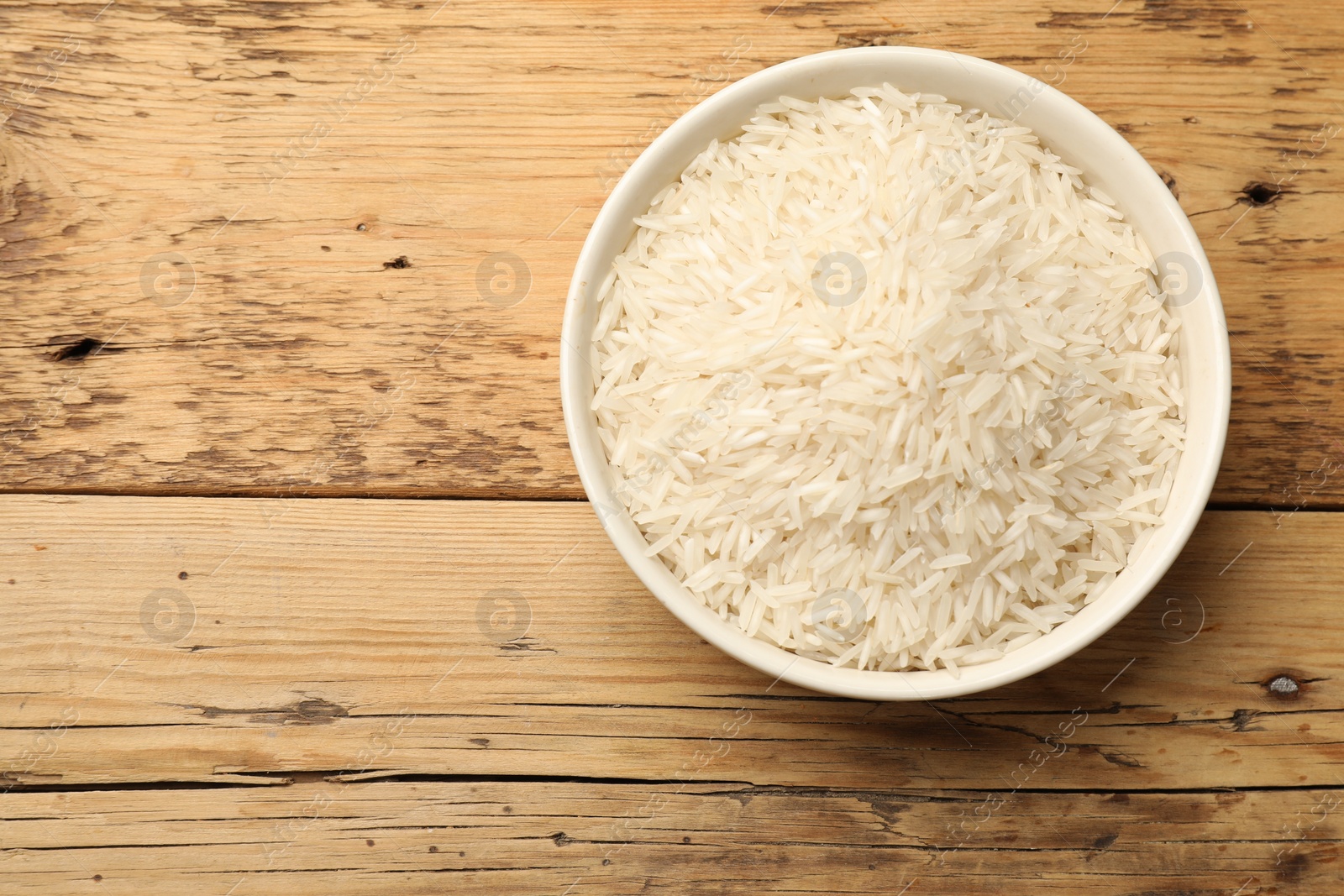 Photo of Raw basmati rice in bowl on wooden table, top view. Space for text