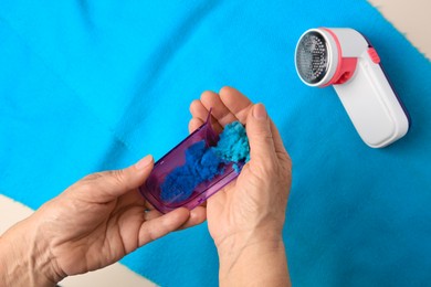 Photo of Woman emptying fabric shaver above light blue cloth on pink background, closeup