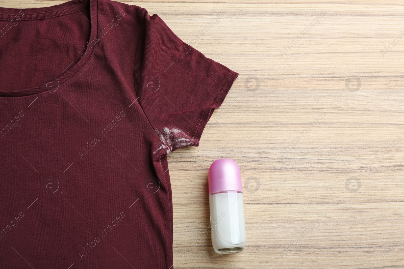 Photo of T-shirt with stain and deodorant on wooden background, top view. Space for text