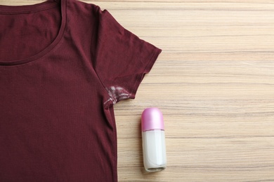 Photo of T-shirt with stain and deodorant on wooden background, top view. Space for text