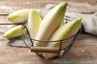 Photo of Fresh raw Belgian endives (chicory) in metal basket on wooden table