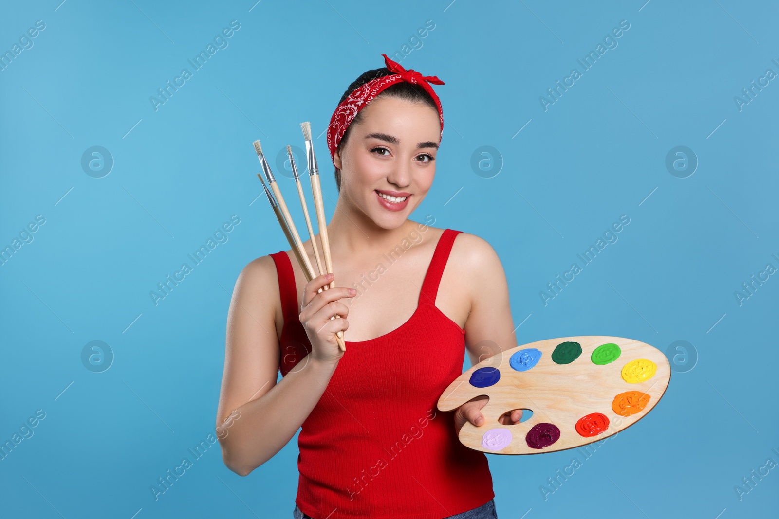 Photo of Woman with painting tools on light blue background. Young artist