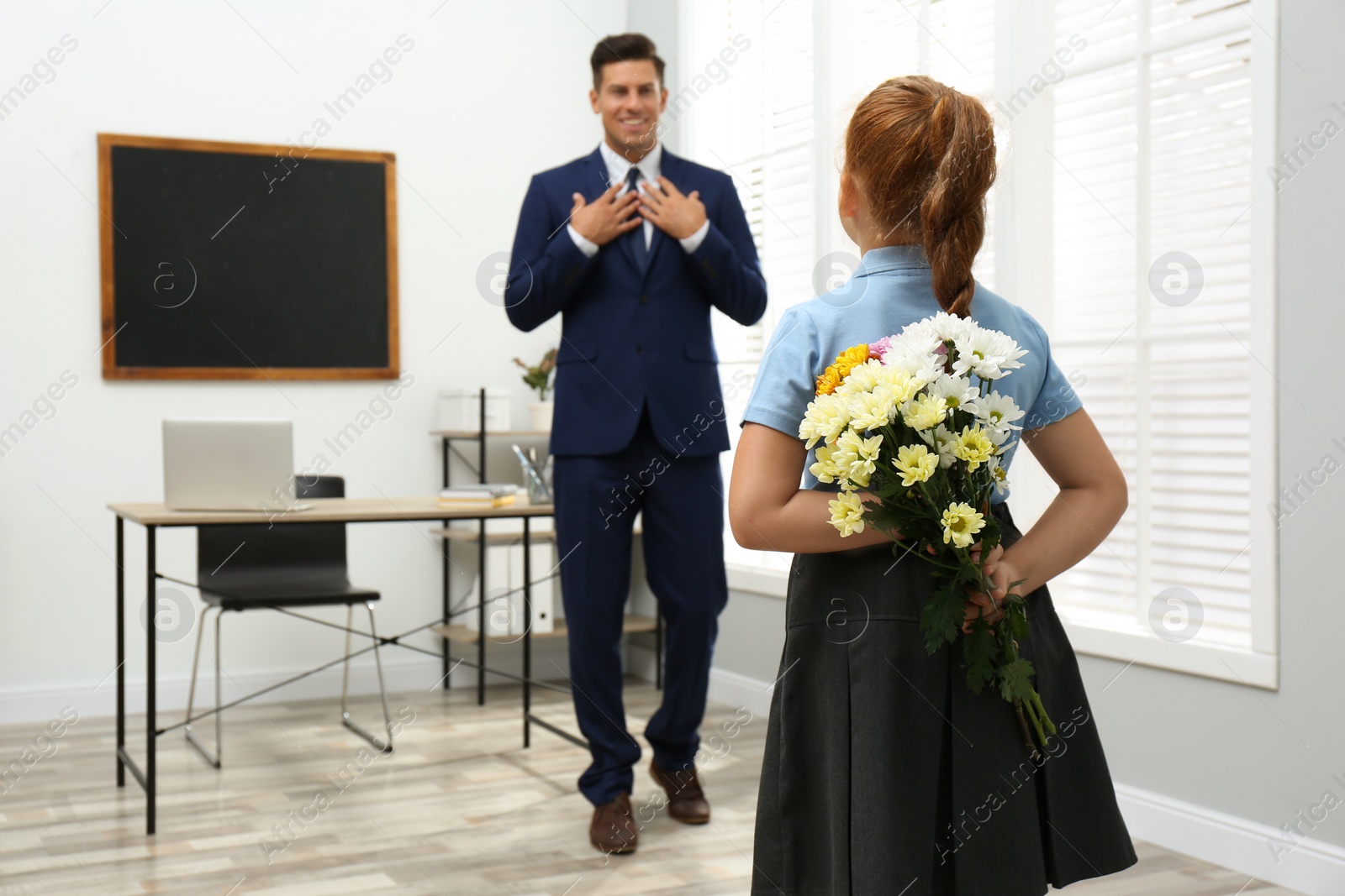 Photo of Schoolgirl with bouquet congratulating her pedagogue in classroom. Teacher's day