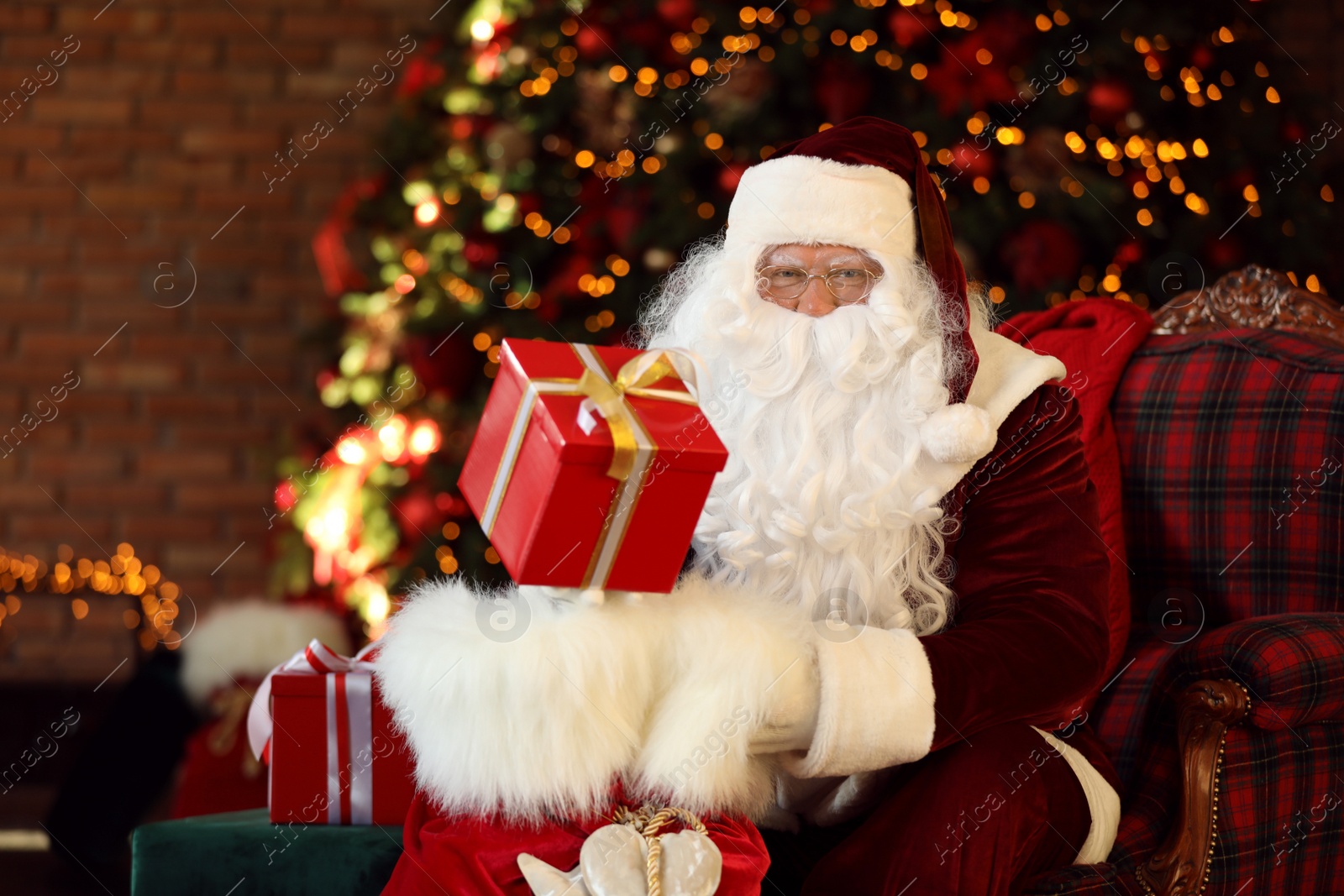 Photo of Santa Claus with gift sack near Christmas tree indoors