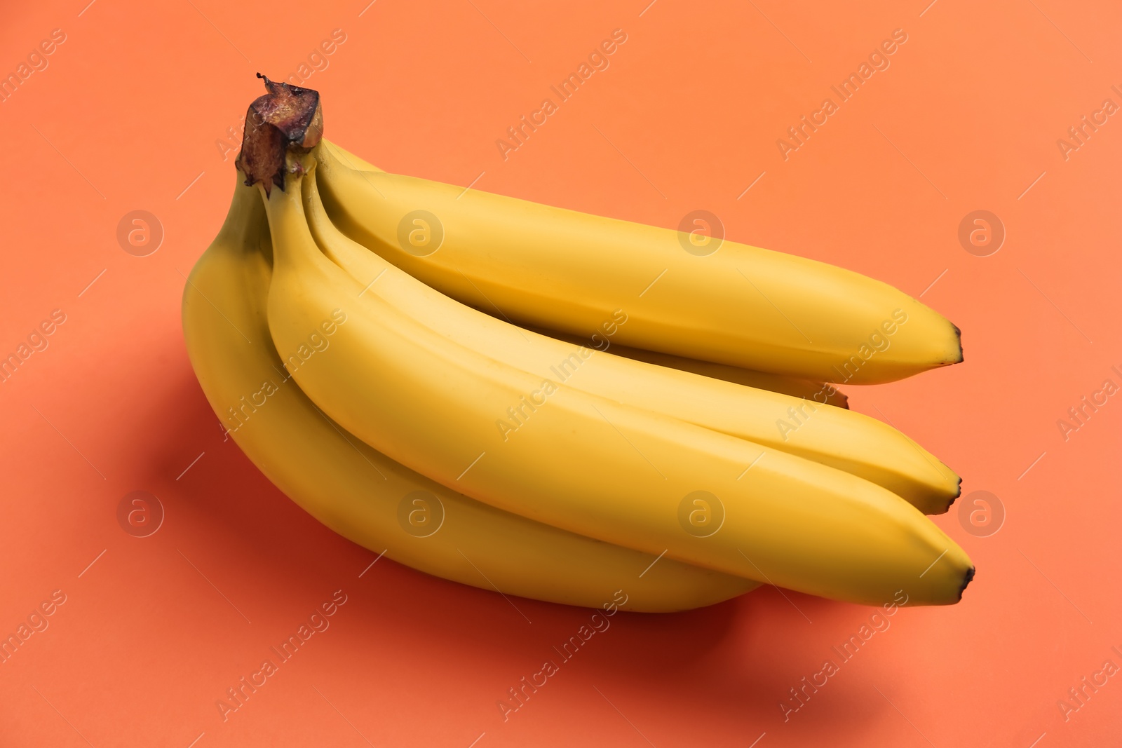 Photo of Bunch of ripe yellow bananas on coral background