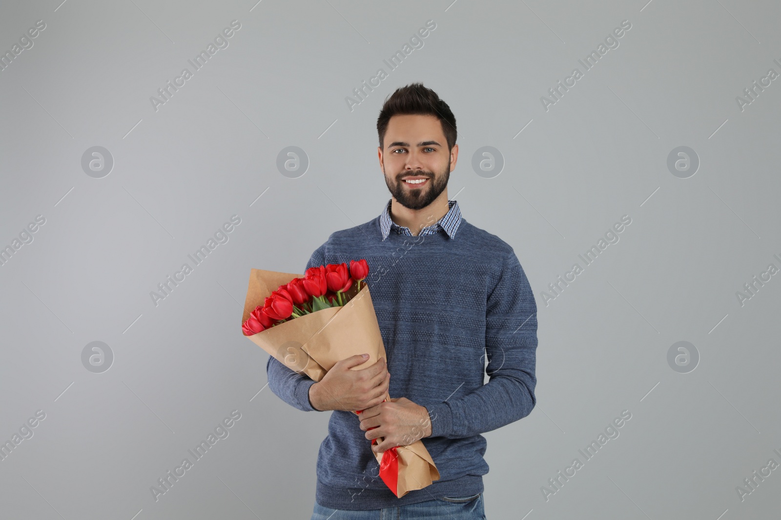 Photo of Happy man with red tulip bouquet on light grey background. 8th of March celebration