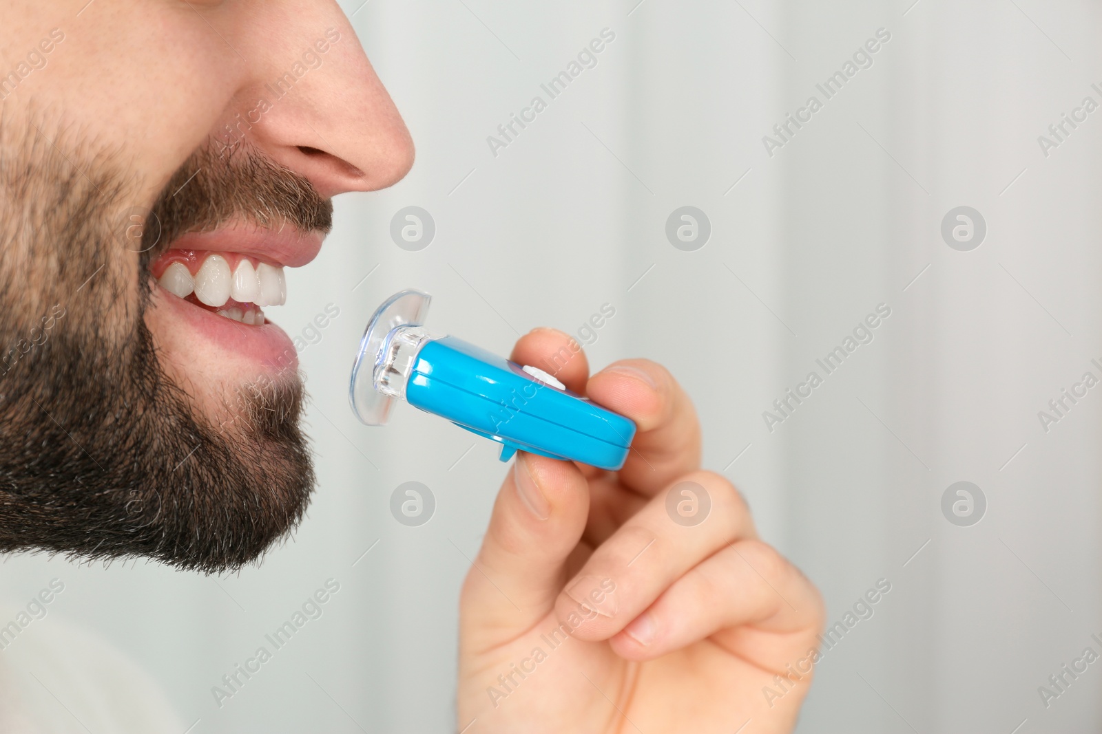 Photo of Young man using teeth whitening device on light background, closeup with space for text