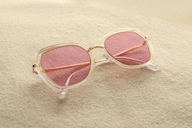 Photo of New stylish sunglasses on sand. Fashionable accessory