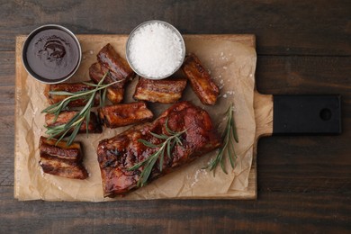 Photo of Tasty roasted pork ribs served with sauce and rosemary on wooden table, top view