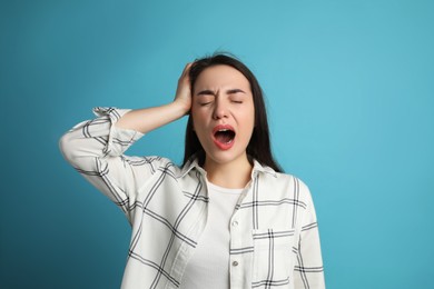 Young tired woman yawning on light blue background