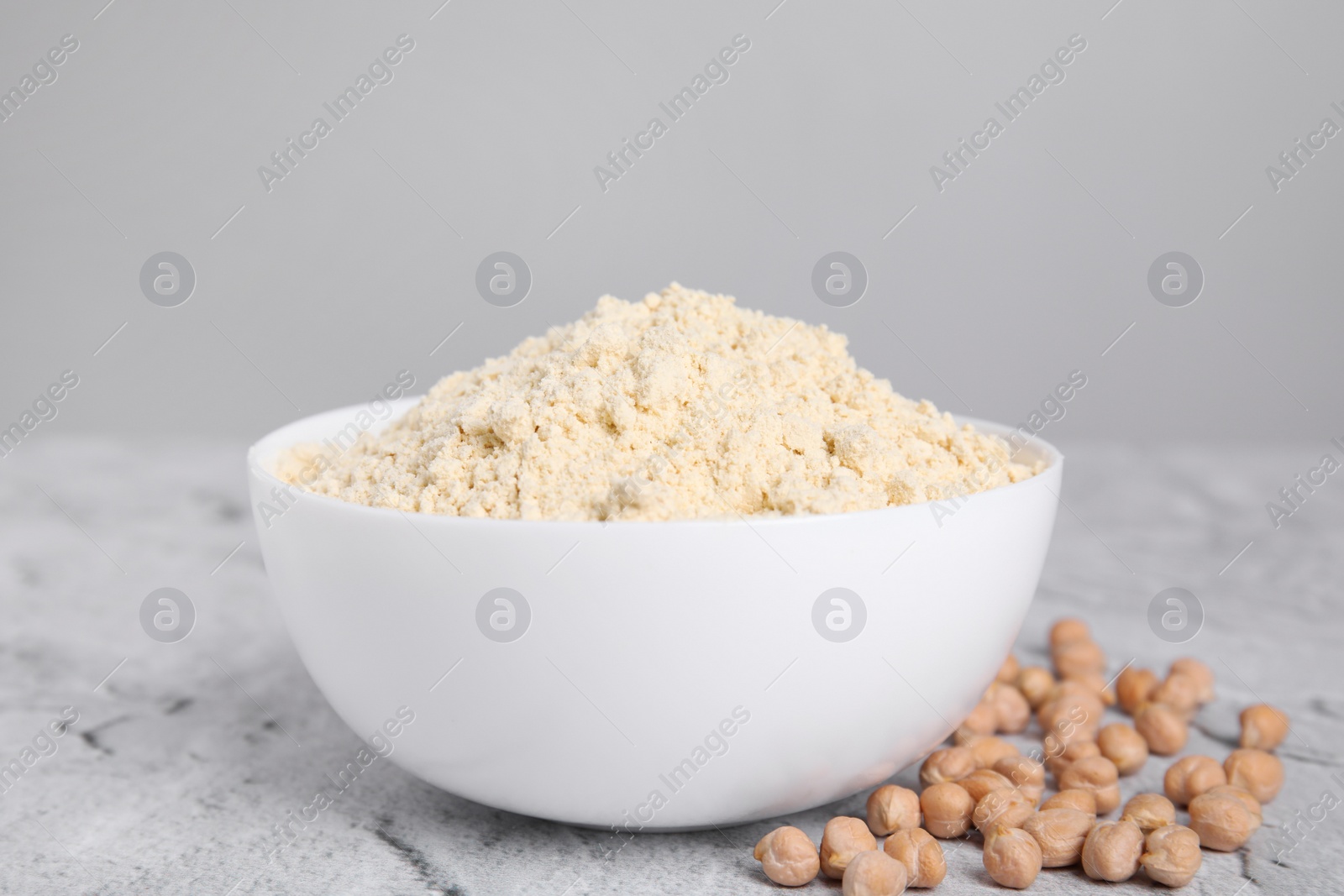 Photo of Chickpea flour in bowl and seeds on light grey textured table