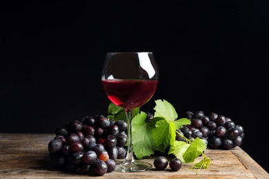 Photo of Fresh ripe juicy grapes and glass of red wine on table against black background