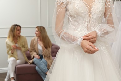 Photo of Bride with friends choosing wedding dress in boutique